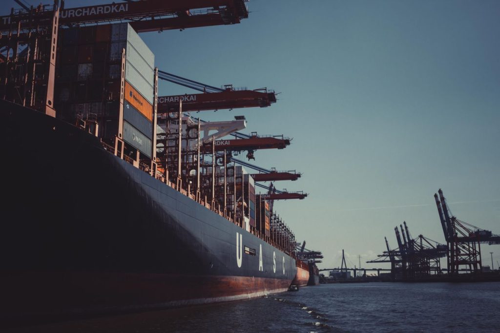 Services A large cargo ship docked at Hamburg Harbor, cranes loading containers under a clear sky.