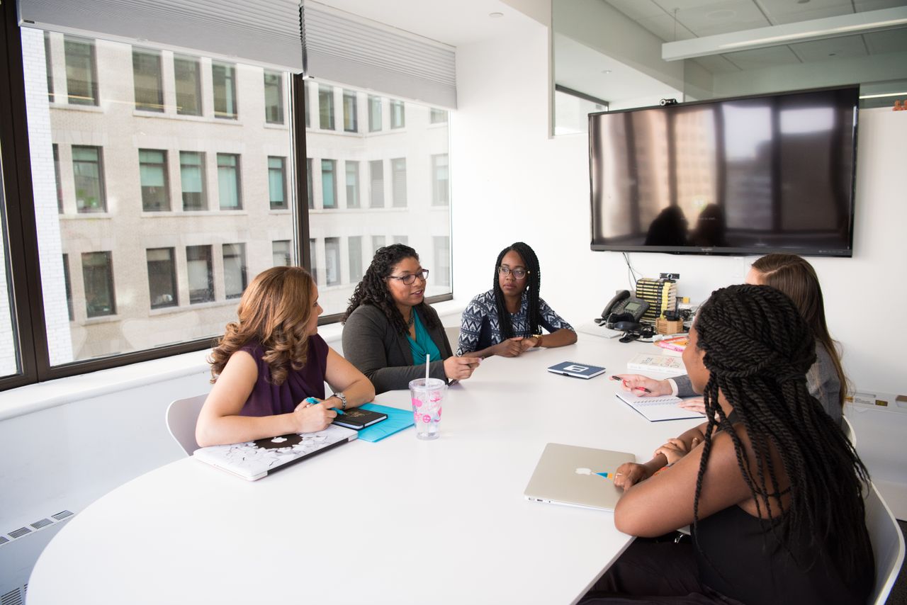 Home A group of diverse women engage in a business discussion in a modern office setting.