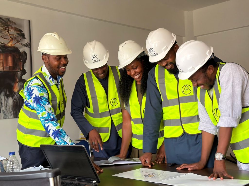 Services Diverse team of African engineers in hard hats and safety vests reviewing building plans indoors.