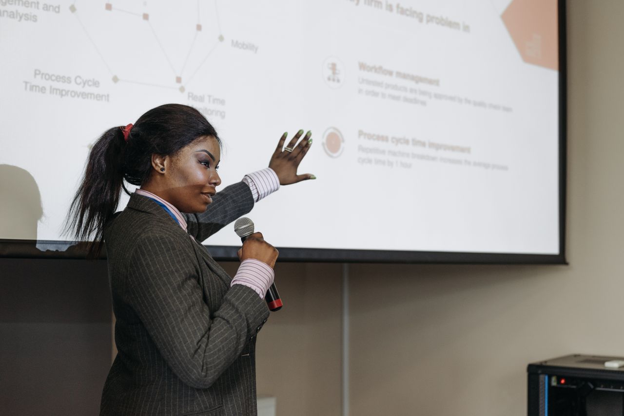Services Businesswoman presenting with microphone, discussing improvements with a slide projection in a conference room.